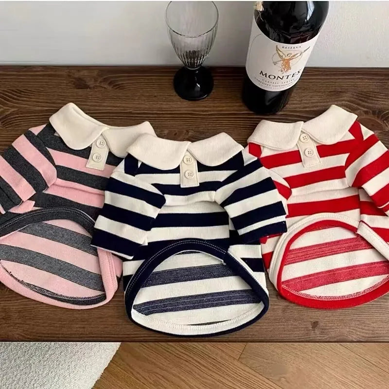 A collection of striped dog hoodies in pink, navy, and red are displayed on a wooden surface.
