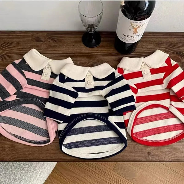 A collection of striped dog hoodies in pink, navy, and red are displayed on a wooden surface.