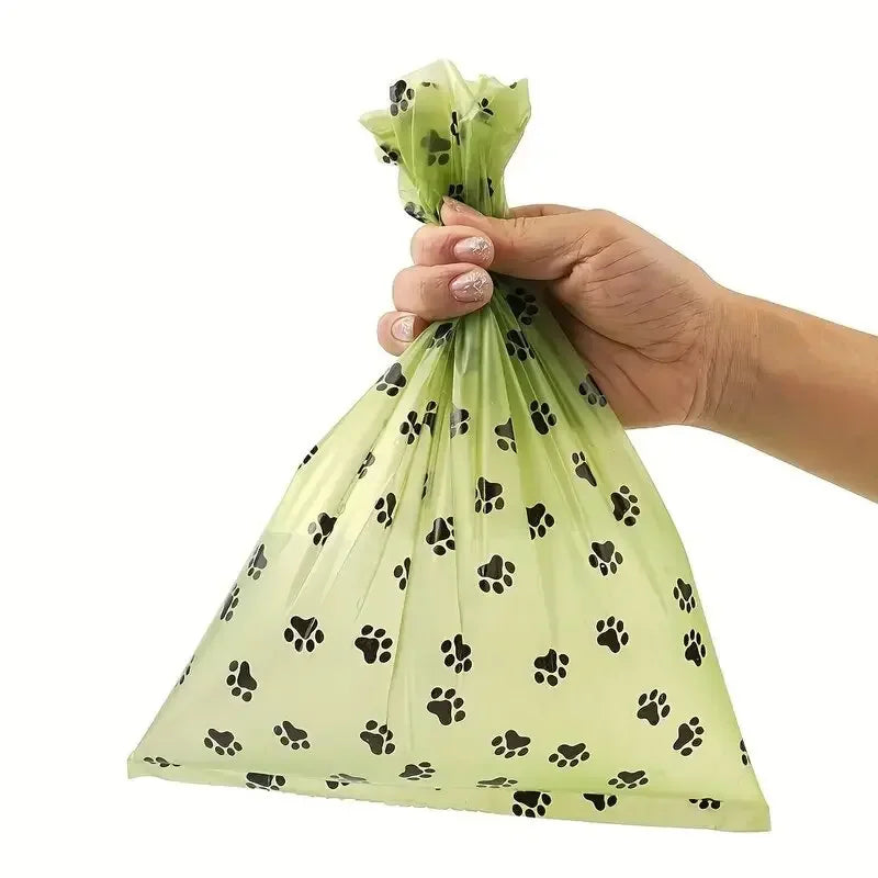 A hand is holding a clear, biodegradable mesh bag filled with black dog poop, showing the product.