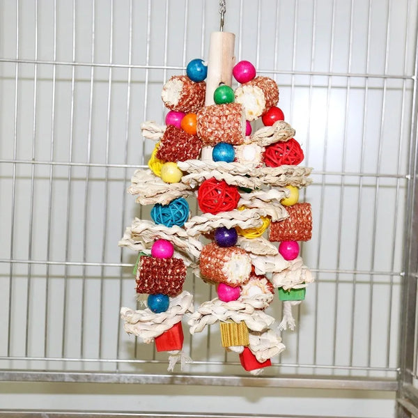 A colorful wooden parrot bite toy made of various candies and fabric wrapped in twine hanging in a wire cage.