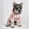 A fluffy gray dog wearing a pink waterproof raincoat and jumpsuit.