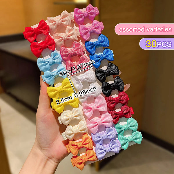 A hand holds a variety of assorted colorful fabric hair clips in various shades of pink, red, blue, and yellow.
