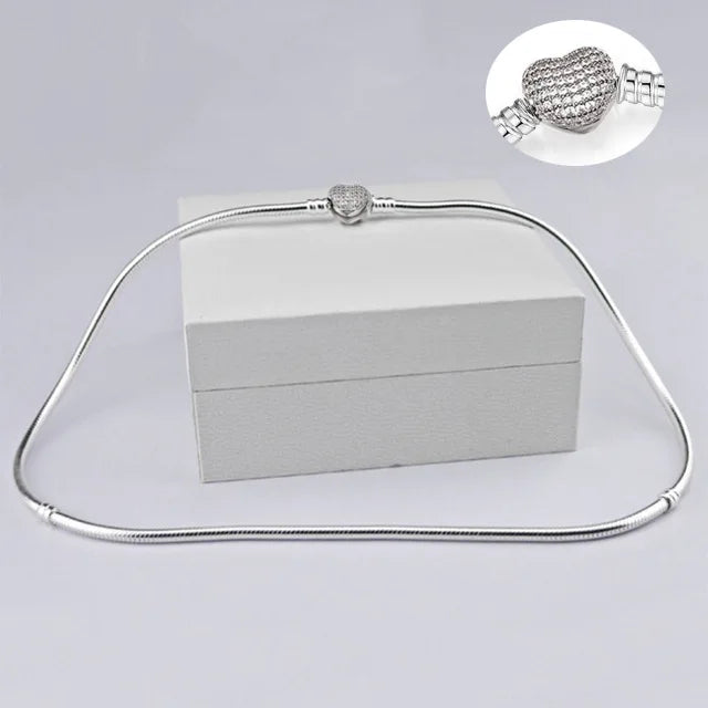 A silver snake chain necklace with a heart charm displayed on a white box.