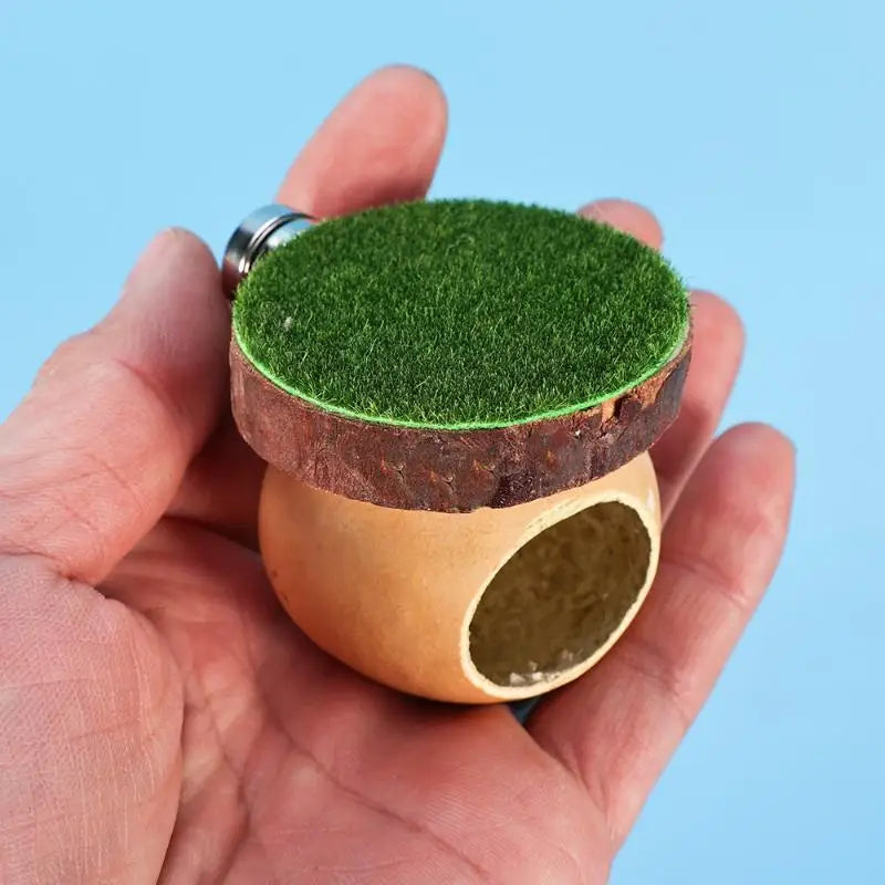 A hand holds a mini magnetic spider hide decor featuring green moss on top and a natural wood base.