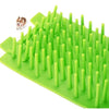 A green silicone pet paw cleaner tool with numerous cylindrical bristles is shown next to a small dog.