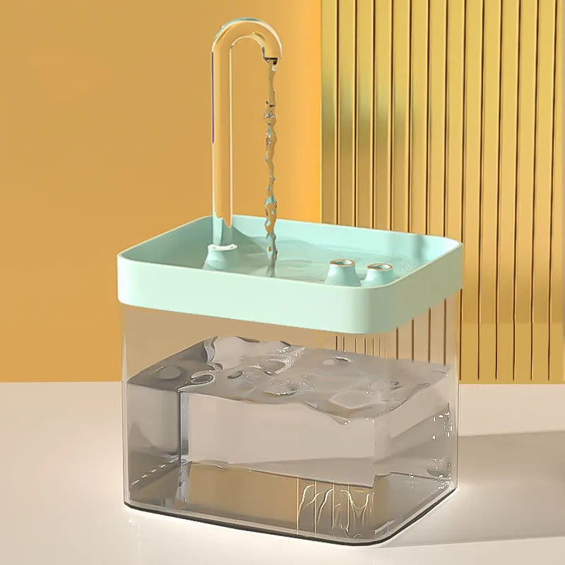 A clear glass water fountain with a light green top and a vertical carbon filter visible inside.