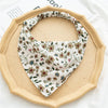 A beige triangle scarf with a floral pattern is displayed on a round wooden tray.