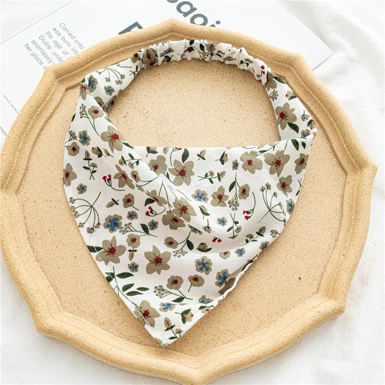 A beige triangle scarf with a floral pattern is displayed on a round wooden tray.