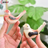 Eine Hand hält eine kleine rosa und schwarze Wasservogelpfeife für Kinder vor einem unscharfen grünen Hintergrund.