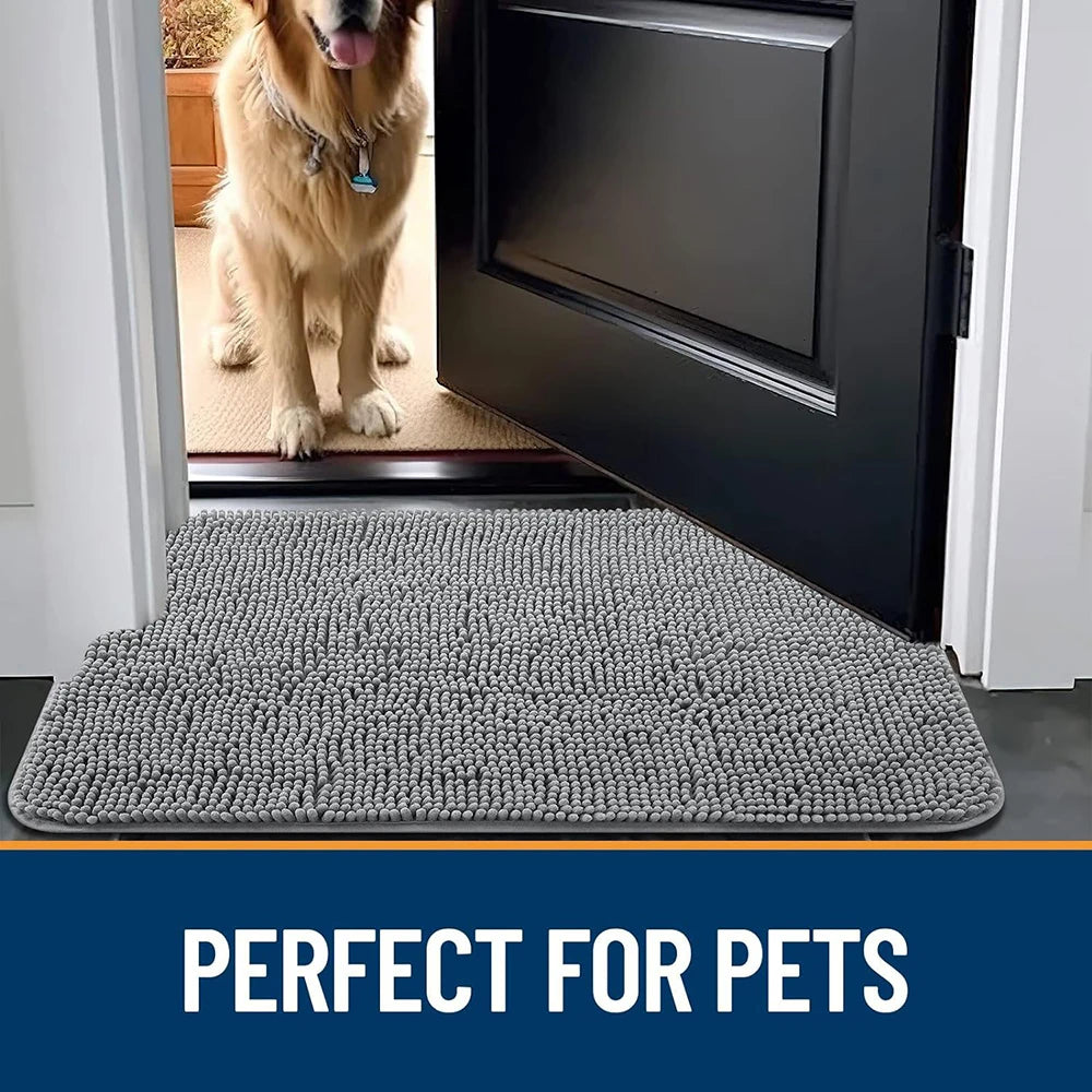 Alfombrilla de goma gris antideslizante para mascotas frente a una puerta negra, con un perro visible al fondo.