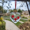 Un abreuvement en forme de cœur en verre transparent avec des fleurs rouges, suspendu à un cordon rouge dans un jardin extéri