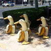 A set of cute resin banana duck garden sculptures standing upright in a paved area.