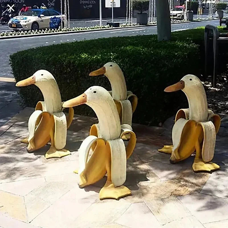 A set of cute resin banana duck garden sculptures standing upright in a paved area.