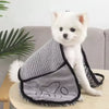 A white dog wearing a gray pet bath towel with black trim sitting on a wooden surface.