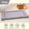 A gray chew-proof pet mat is shown on a white blanket with a teddy bear and a small pink device.