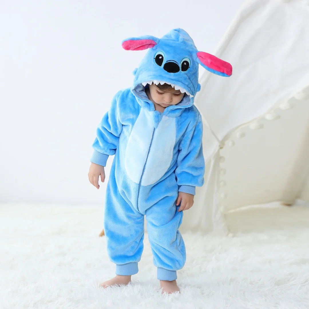 A baby wearing a blue cartoon animal hooded romper with pink ears, standing on a white surface.