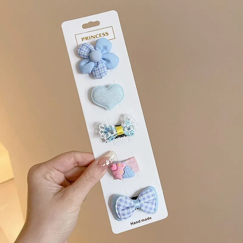 A hand holds a white card displaying five handmade flower-shaped baby hair clips in various shades of blue and pink.