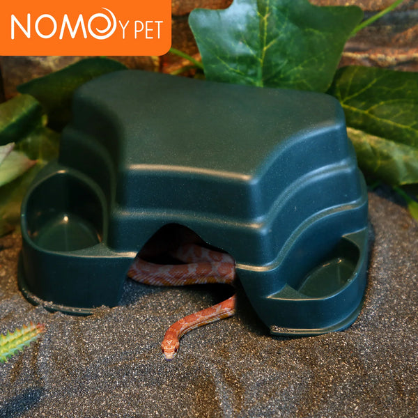 A dark green reptile hide cave decoration with food bowls, featuring a small snake inside.