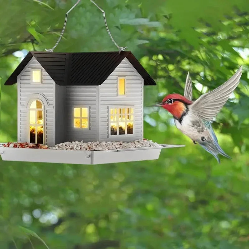 A solar outdoor bird feeder lantern shaped like a small house, with a bird flying near it in a green outdoor setting.