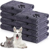 A stack of gray pet bath towels with paw print designs next to a dog and a cat.