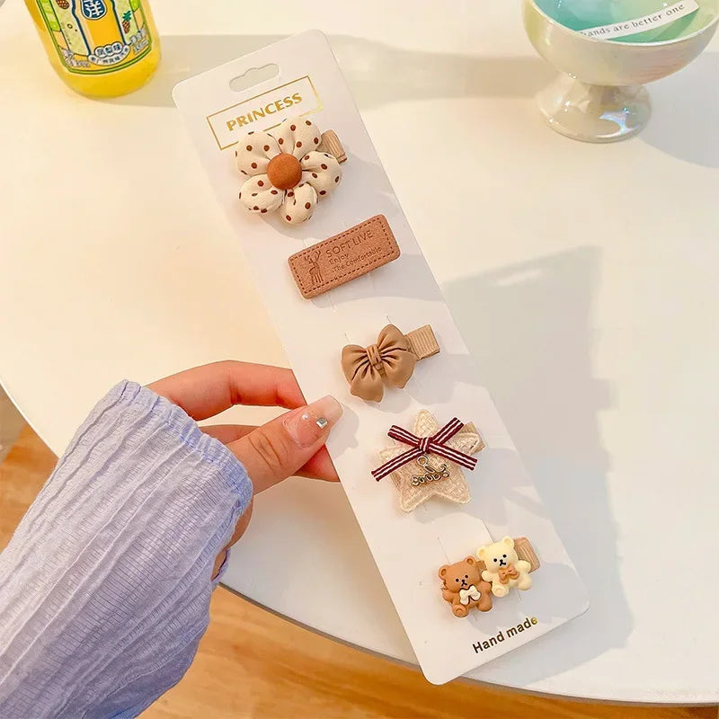 A hand holds a white card displaying five handmade flower-shaped baby hair clips on a light surface.