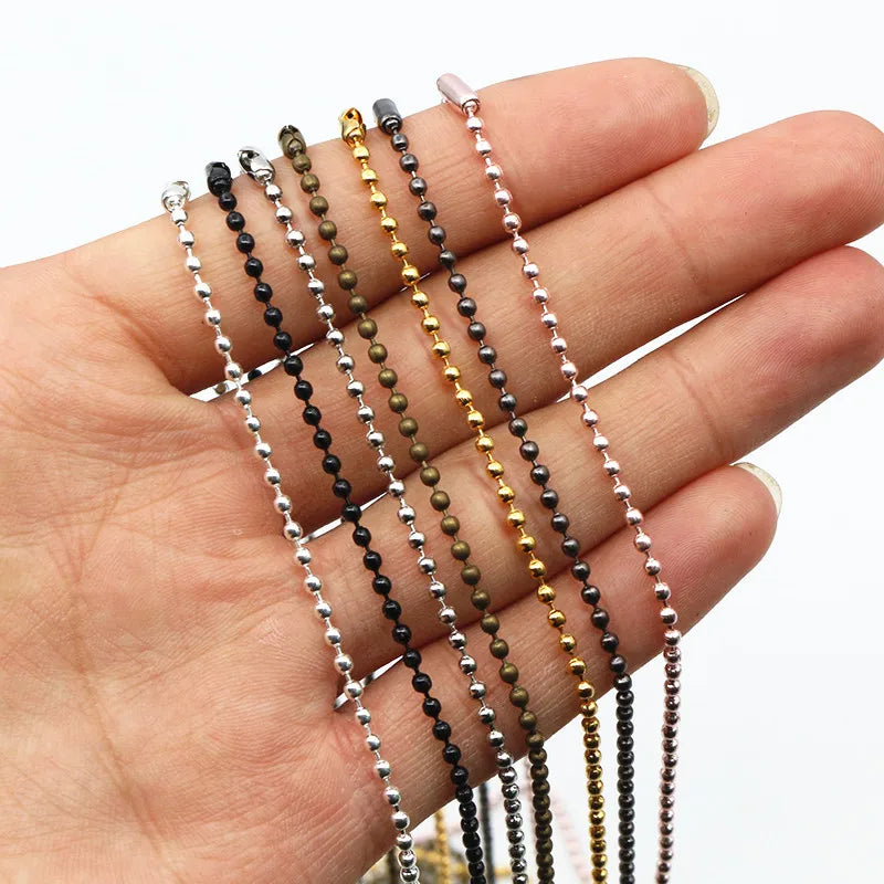 A hand holds a set of plated ball bead necklaces in various colors including black, gold, and olive green.
