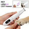 Una mano sostiene una recortadora de pelo para mascotas blanca con luz LED/UV, demostrando su uso en la pata de un perro.