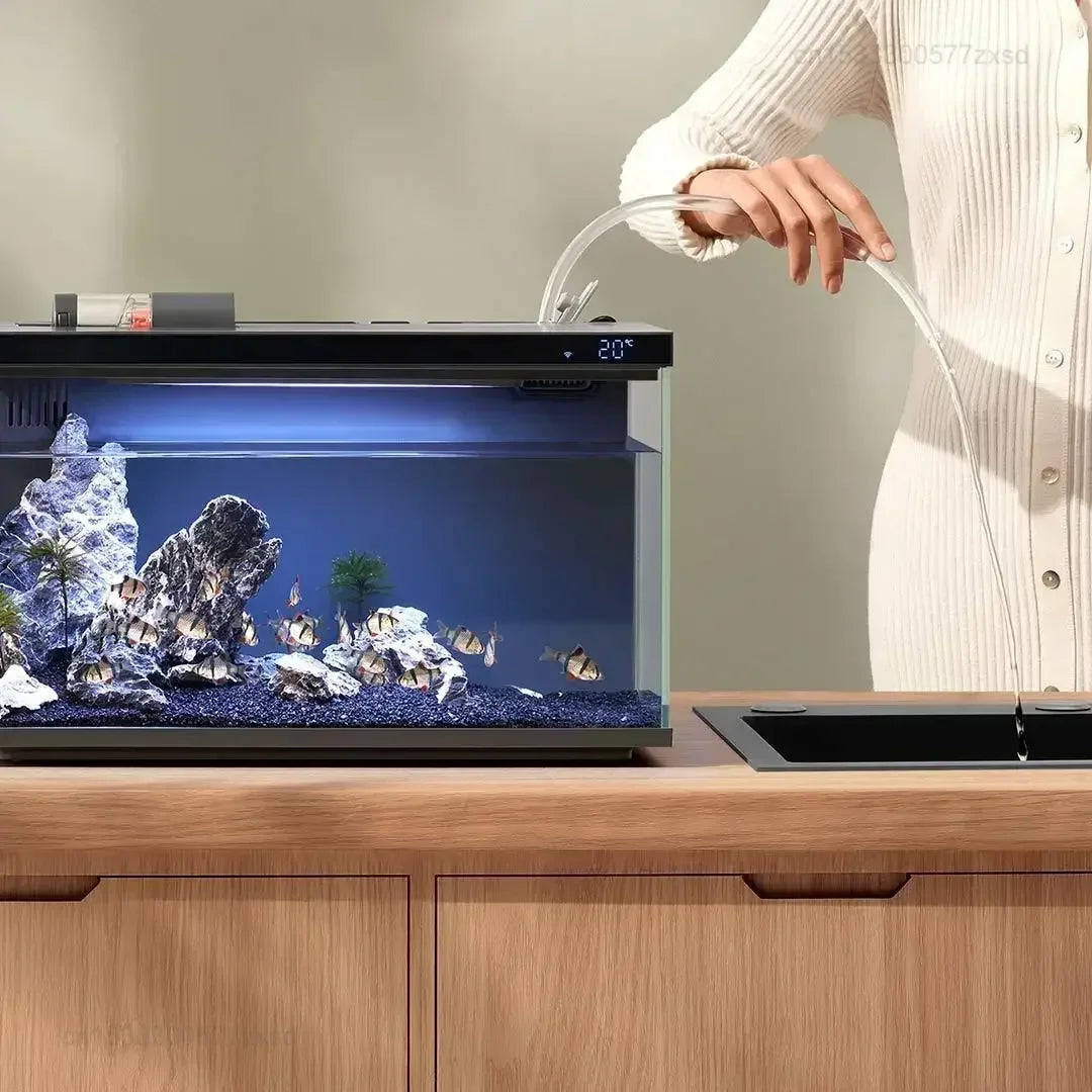 Une personne utilise un tube transparent pour nourrir un poisson dans un aquarium en verre posé sur un comptoir en bois.