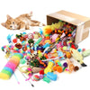 A bundle of mixed cat play toys including feathers, yarn, and small accessories next to a cardboard box and a kitten.