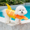 A fluffy white dog wearing a bright orange and yellow high visibility life vest next to a blue swimming pool.