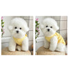A fluffy white dog wearing a yellow waffle knit pet vest, sitting on a woven mat.