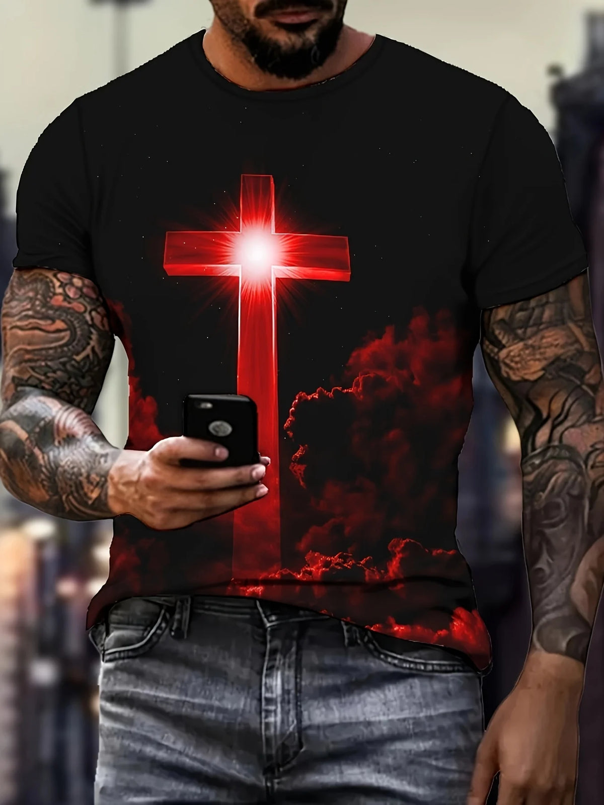 A man wearing a black t-shirt with a red cross design and flames, holding a smartphone.
