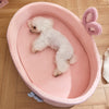 A fluffy white dog is resting inside a pink pet bed with a removable cover and raised guardrail.