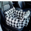 A plaid pet car seat with safety straps is placed in a dark car interior.