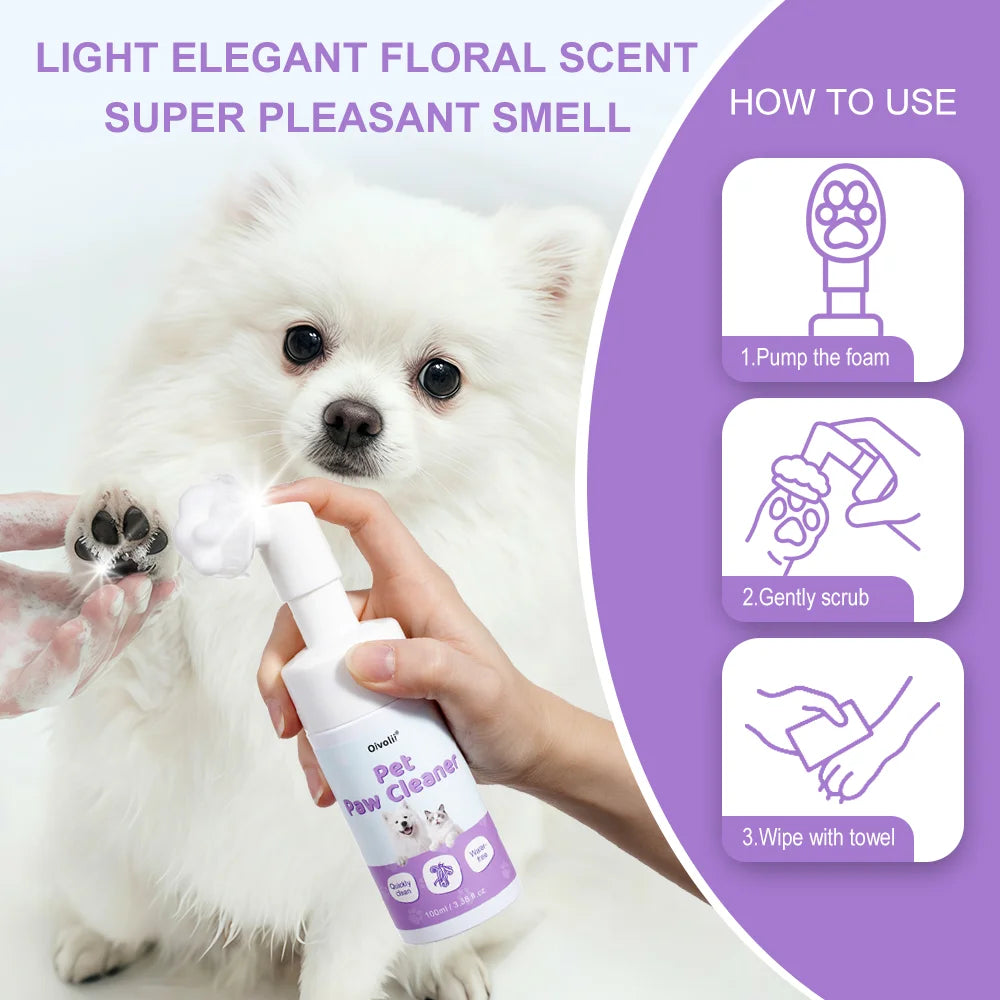 A person is using a white spray bottle of Pet Paw Cleaner to gently scrub a white dog's paw.