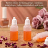 Two small glass dropper bottles filled with orange liquid sitting on a wooden surface surrounded by dried rose petals.