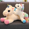 A soft, light yellow unicorn plush toy with a rainbow mane and colorful accents is lying on a dark gray surface.