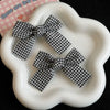 A pair of black and white plaid fabric bow hair clips displayed on a white ceramic dish.