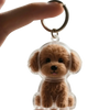 Un pequeño y peludo charm de perro marrón unido a un anillo de llavero de plata.