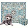 A fluffy gray dog is lying in front of a patterned blue and cream reusable dog pee pad.