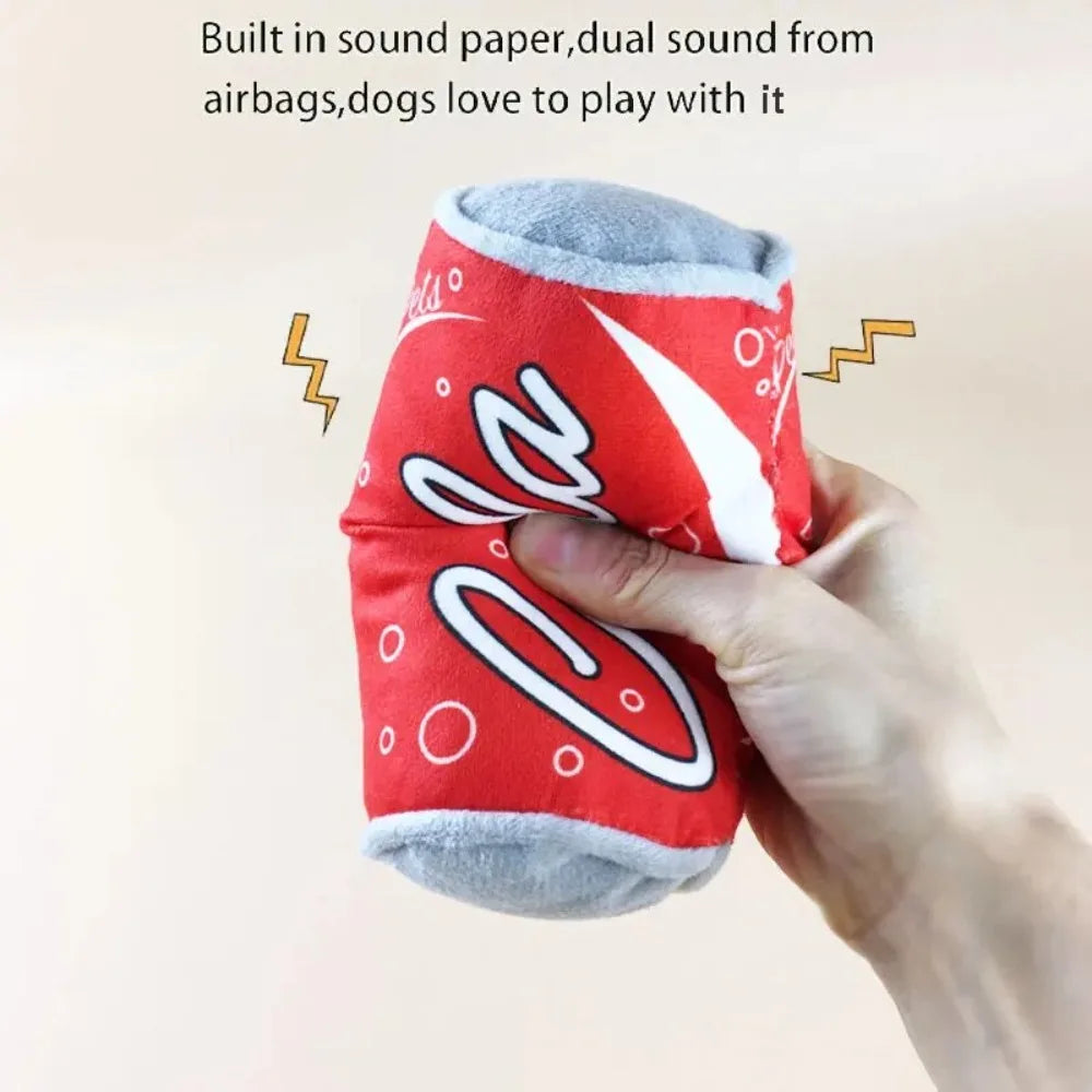 A hand holds a red and gray bottle-shaped squeaky plush dog toy with lightning bolt graphics.