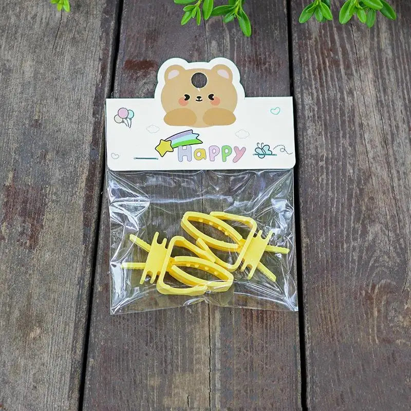 A clear plastic bag contains yellow clip-on bird cage feeder cups with mounting brackets and a happy bear sticker.