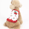 A fluffy brown dog wearing a white vest with red cherry embroidery and a ruffled red trim.