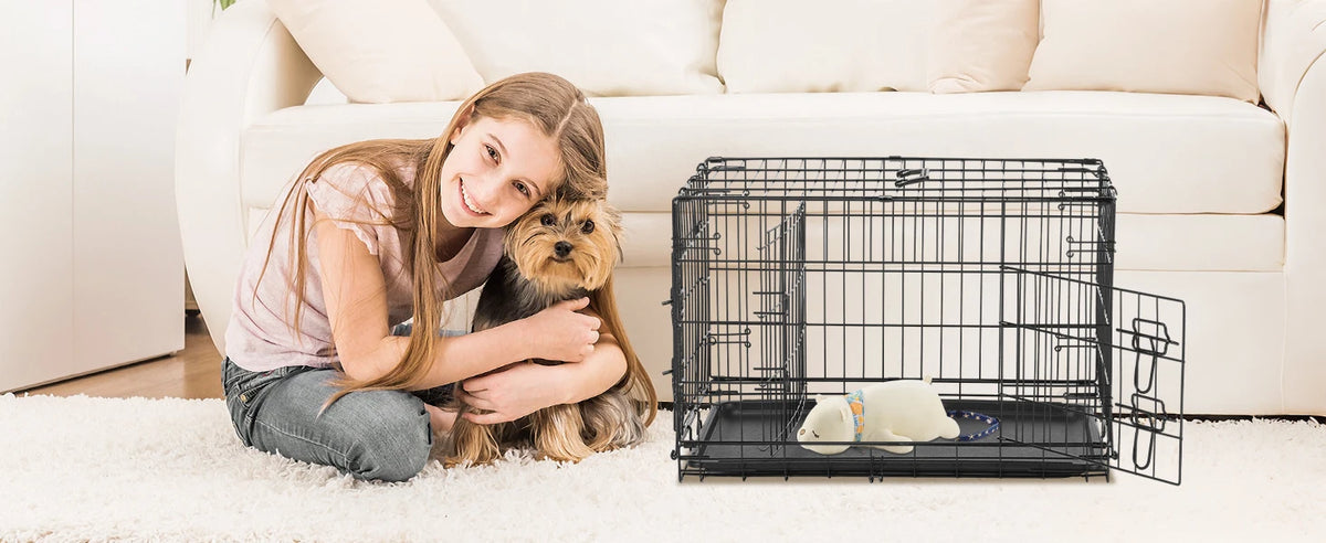 Una niña está sentada en un sofá blanco con un perro junto a una jaula de transporte plegable extra grande.