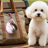 Ein flauschiger weißer Hund sitzt neben einer braunen Tasche mit einem rosa Edelstahl-Wasserdispenser.