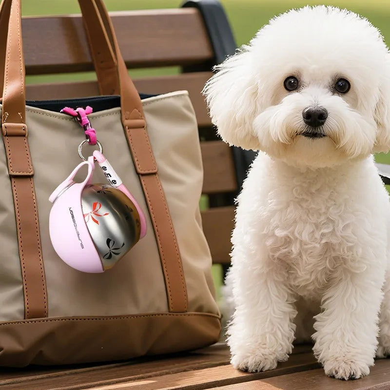 Ein flauschiger weißer Hund sitzt neben einer braunen Tasche mit einem rosa Edelstahl-Wasserdispenser.