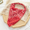 A red paisley triangle head scarf is displayed on a beige woven mat with a white lace cloth in the background.