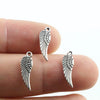 A hand holds several antique silver wing charms, showing their detail and size.