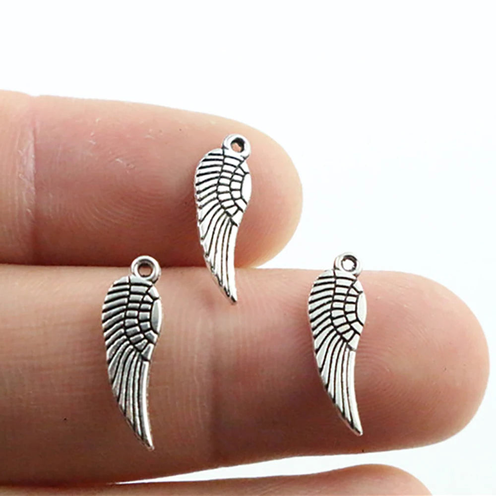 A hand holds several antique silver wing charms, showing their detail and size.
