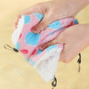A hand is holding a pink and blue plush pet hammock for small animals, showing its soft texture and attached loops.